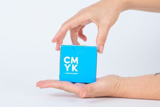 Main tenant un petit cube bleu avec le texte "CMYK" sur un fond gris clair