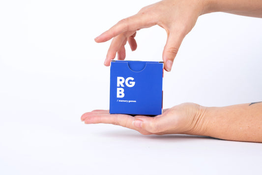 Cube bleu avec texte "RGB" et "jeu de mémoire" tenu dans une main sur fond blanc